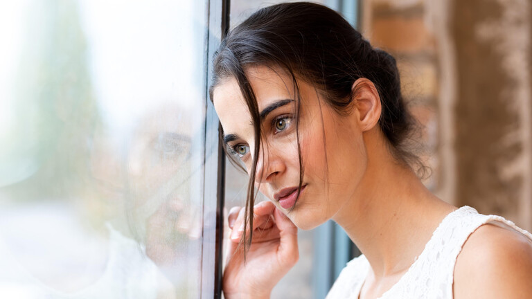 Eine Frau blickt sehnsuchtsvoll aus dem Fenster.