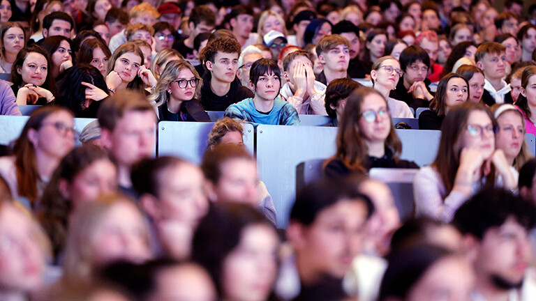 In einem Hörsaal sitzen viele Studierende, sie blicken alle nach vorne.
