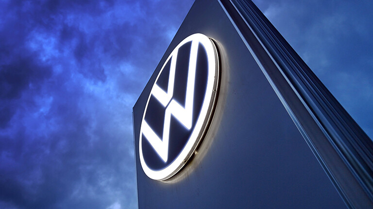 Das Volkswagen-Logo auf einer Steele vor dunklem Himmel mit vielen Wolken.