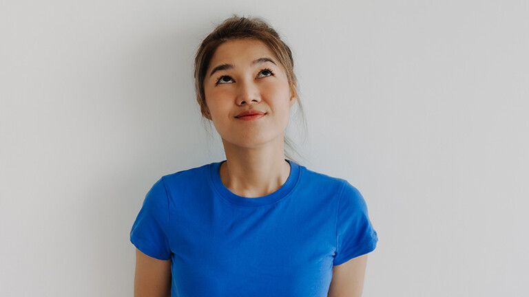 Eine Frau mit blauem T-Shirt blickt nach oben und schaut fragend.