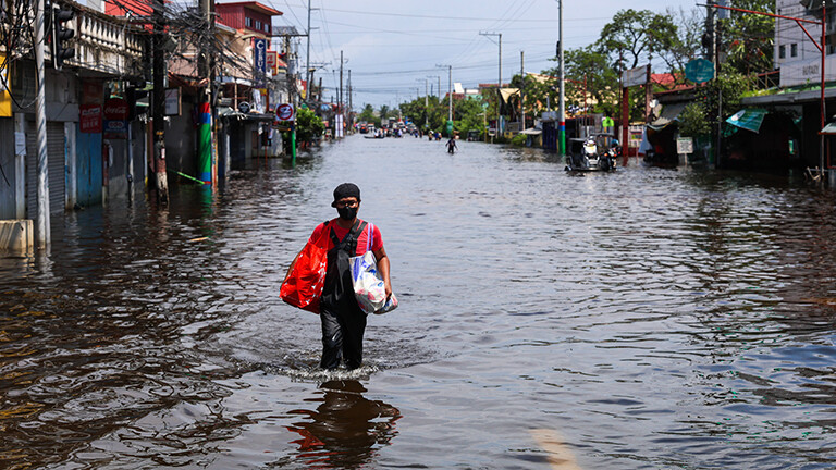In Pampanga, in den Philippinen, geht ein Mann über eine Straße, die unter Wasser steht. Er trägt zwei Taschen bei sich.