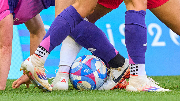 Szene im Frauenfußball bei der olympischen Halbfinalpartie Deutschland gegen die USA 2024. Zu sehen sind die Beine von drei Spielerinnen, die um den Ball kämpfen.
