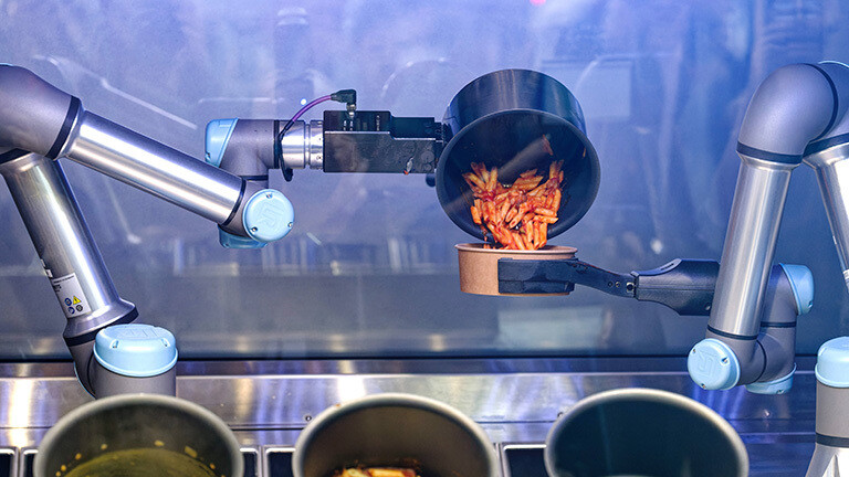 Eine Roboterarm kippt ein vom autonomen KI-Kochroboter CA-1 Nudelgericht in eine Schüssel.