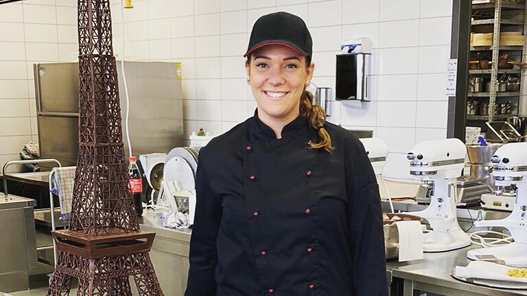 Eine Frau mit einer Cappy steht neben einem Eifelturm aus Gebäck.