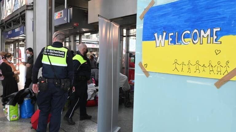 Mitarbeiter der DB-Sicherheit steht am Münchner Hauptbahnhof neben einem selbstgemalten Bild mit ukrainischer Flagge, der Aufschrift „welcome“ sowie Strichmännchen und einem Herzen (11.03.2022)