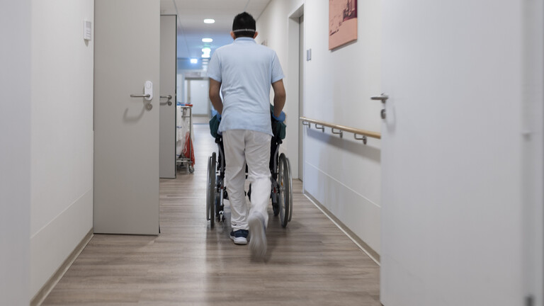 Ein Pfleger schiebt einen Rollstuhl durch einen Gang im Pflegeheim