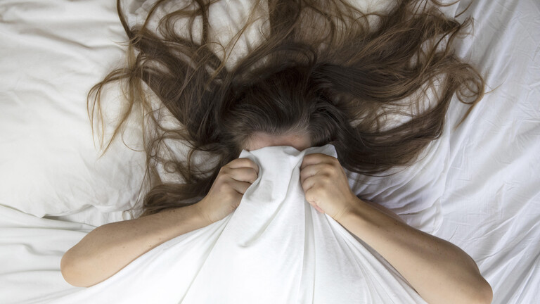 Eine Frau zieht sich im Bett die Decke über im Kopf