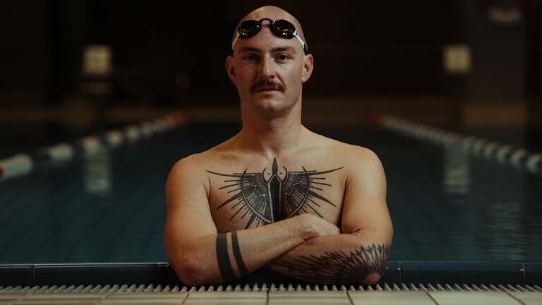 Ein Mann im Schwimmbecken verschränkt die Arme vor der Brust und blickt in die Kamera.