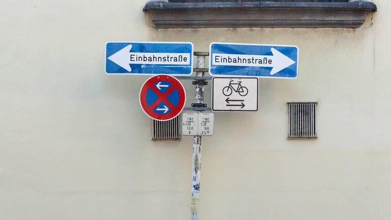 Ein Fahrrad parkt unter sich scheinbar widersprechenden Verkehrsschildern