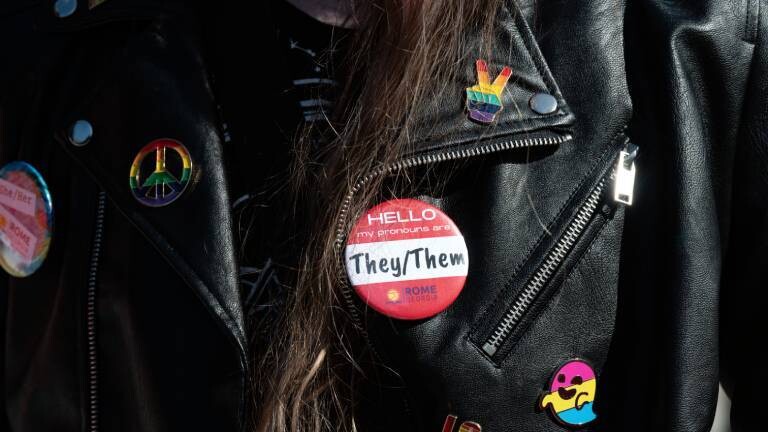 Eine Person trägt einen Butten mit der Aufschrift "They/Them"
