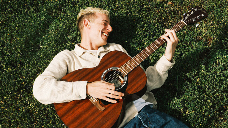 Shelter Boy mit seiner Gitarre im Grünen.