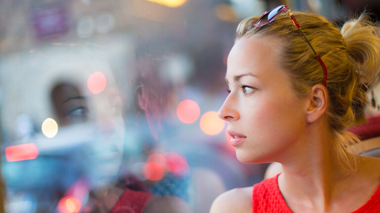 FRau schaut aus dem Fenster, es spiegelt sich ihr Gesicht.
