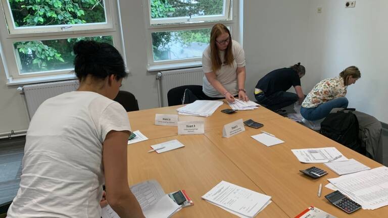 Wahlhelfer üben das Auszählen an Tischen, auf denen Wahlzettel liegen.