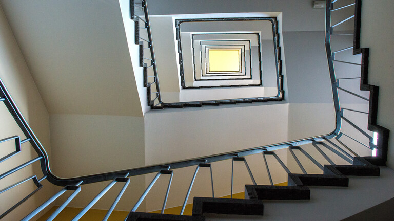 Blick aus der Froschperspektive in ein Treppenhaus mit weißen Treppen und schwarzem Geländer