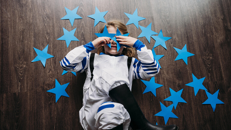 Girl wearing space costume covering eyes with blue stars lying on floor at home