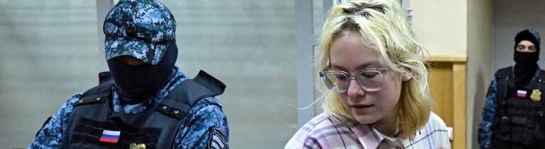 Diana Loginowa vor Gericht in St. Petersburg, neben ihr steht ein vermummter russischer Polizist  (11.11.2025)