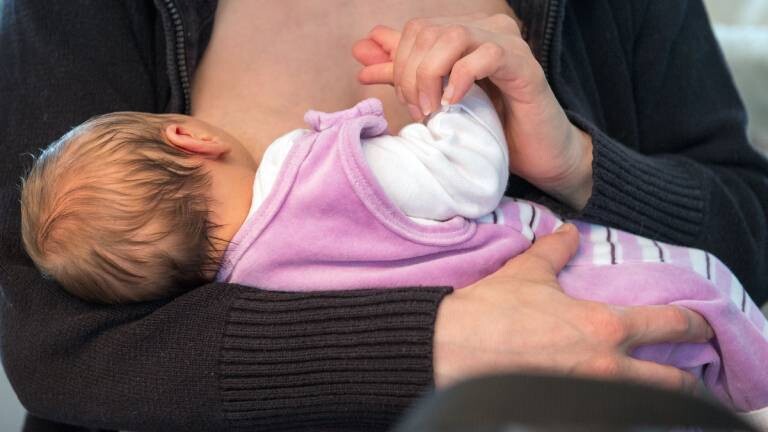 Eine stillende Mutter hält die Hand ihres Kindes.