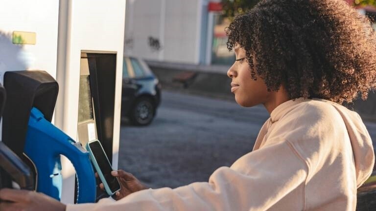 Eine junge Frau zahlt mit ihrem Smartphone an einer Tankstelle