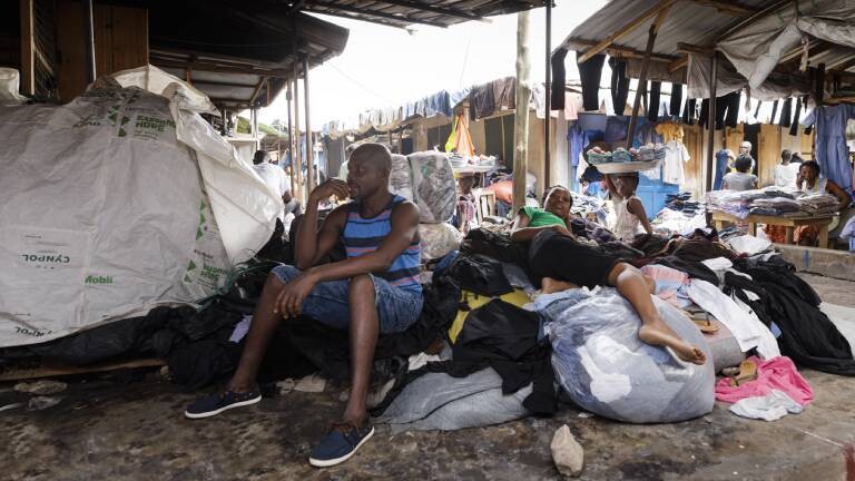 Kantamanto Second-Hand-Textilmarkt in Ghana, Accra. Hier werden Textilien aus der ganzen Welt weiterverarbeitet, verkauft. Verkäufer sitzen an Ständen auf in weißen Säcken verpackte Kleider.