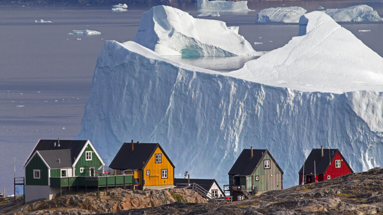 Grönländische Holzhäuser vor Eisberg im Hintergrund