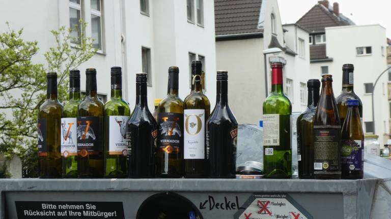 Zahlreiche leere Alkoholflaschen stehen auf einem Glascontainer in einer Siedlung.