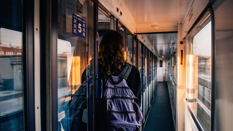 Eine Frau trägt einen Rucksack und steht im Gang eines Nachtzuges. Wir sehen sie von hinten.