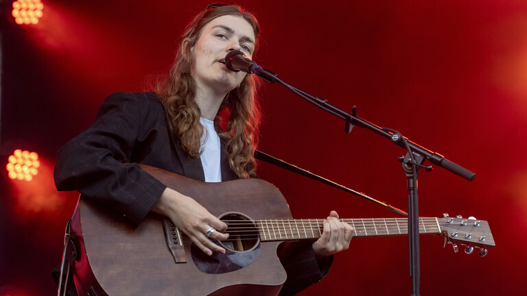 Musikerin Philine Sonny steht bei einem Festival auf der Bühne. Sie singt in ein Mikrofon und spielt dabei ihre Gitarre.