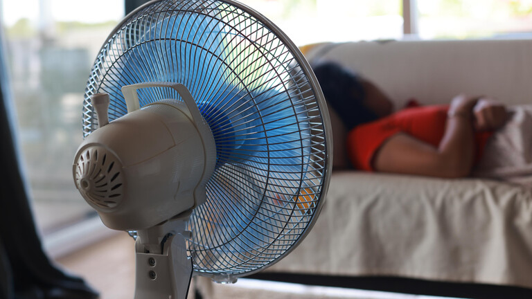 Eine Frau schläft auf einer Couch, im Vordergrund ein Ventilator