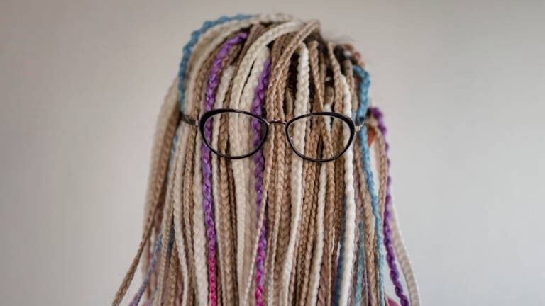 Eine Person mit vielen geflochtenen Zöpfen und einer Brille, das Gesicht ist nicht zu erkennen