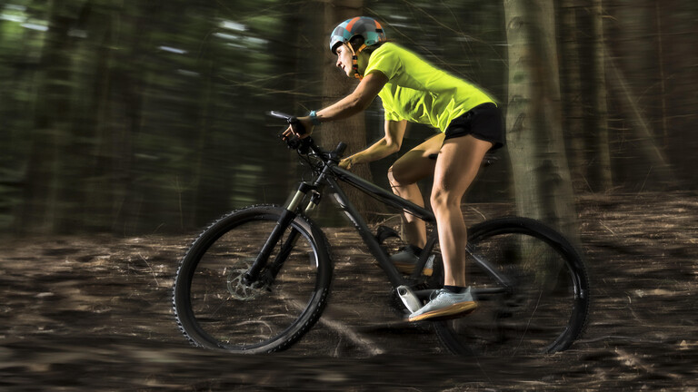 Athletische Mountainbikerin fährt durch den Wald.