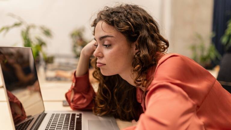 Eine Frau schaut gelangweilt auf einen Laptop