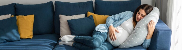 Eine schwangere Frau schläft auf einem Sofa im Wohnzimmer.