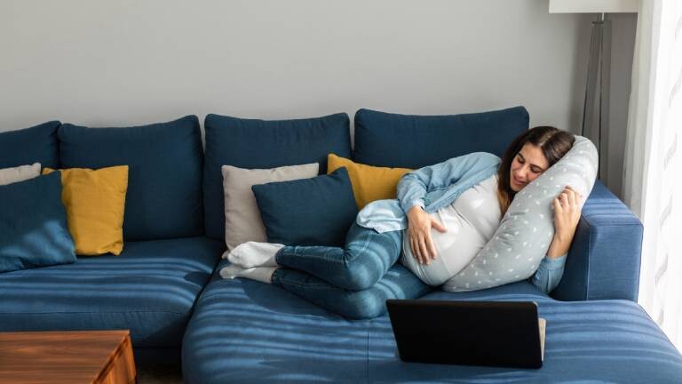 Eine schwangere Frau schläft auf einem Sofa im Wohnzimmer.