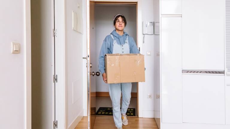 Eine junge Frau trägt einen Umzugskarton in eine Wohnung