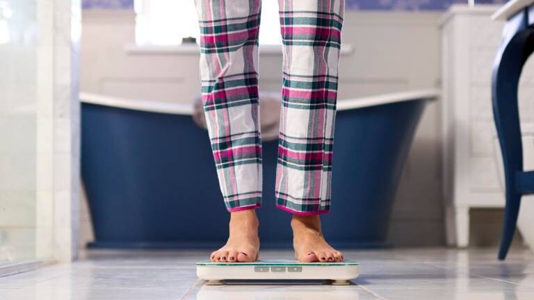 Eine Frau in Pyjama steht auf der Körperfettwaage in ihrem Badezimmer.