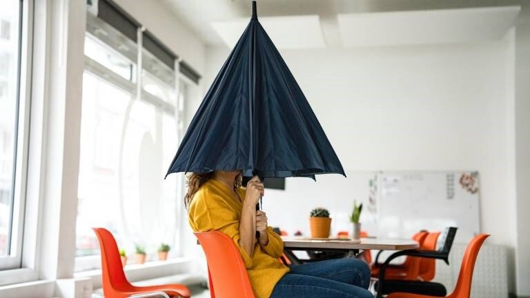 Kreative Geschäftsfrau mit gefaltetem Regenschirm, der das Gesicht am Arbeitsplatz bedeckt