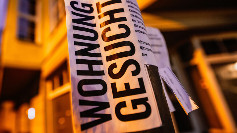 Ein Zettel mit der Aufschrift „Wohnung gesucht“ hängt vor Wohnhäusern.
