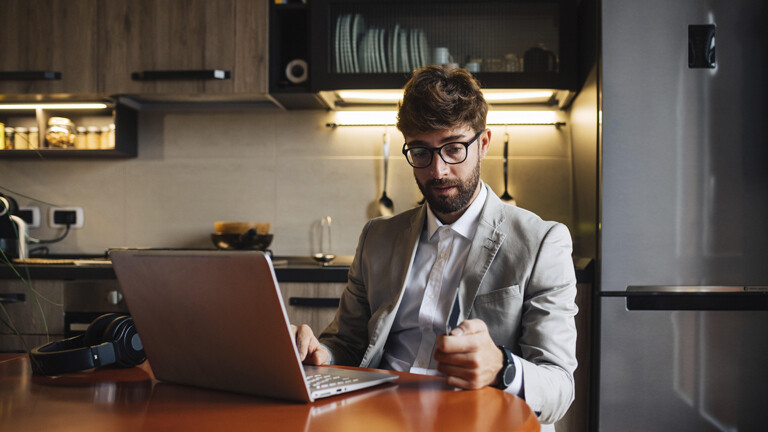 Mann mittleren Alters sitzt am Küchentisch mit Laptop und Kreditkarte.