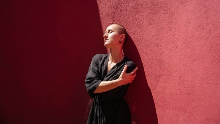 Eine Frau steht vor einer roten Wand und umarmt sich selbst