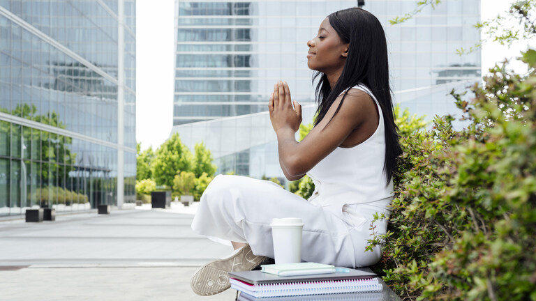 Eine Frau sitzend in Yogaposition seitlich fotografiert mit geschäftlichen Unterlagen und Kaffee
