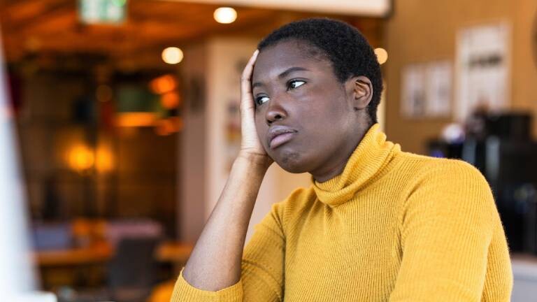 Frau sitzt genervt am Schreibtisch und stützt ihren Kopf auf dem Arm ab