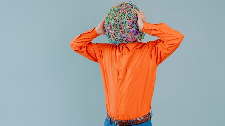 Tired businessman with mask of chaotic thoughts relaxing near blue wall