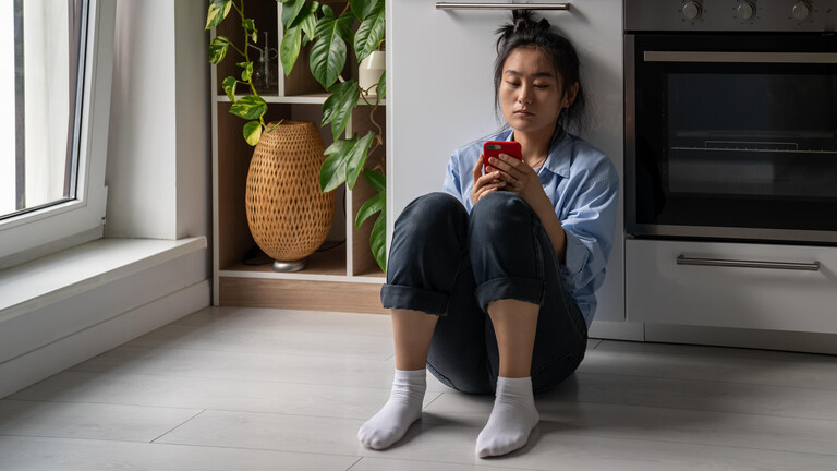 Eine Frau hält ihr Handy in der Hand und blickt mit ernstem Blick auf das Display.