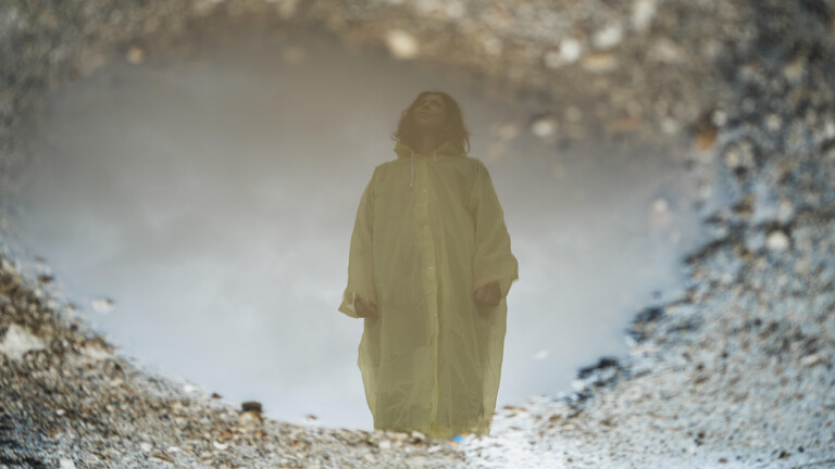 Eine Frau in Regenjacke spiegelt sich in einer Pfütze