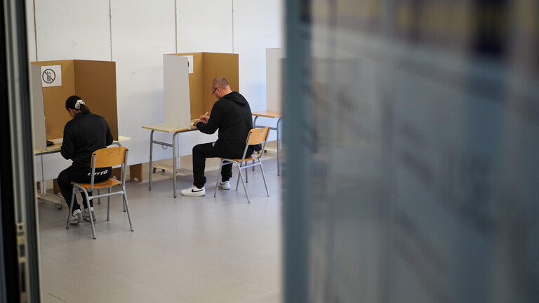 Bei Wahlen in Bosnien und Herzegowina sitzen Menschen in einer Wahlkabine und füllen den Stimmzettel aus. Wir sehen sie von hinten.