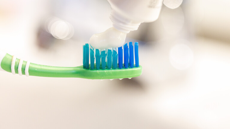 Zahnbürste, auf die jemand Zahnpasta gibt