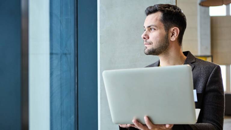 Mann mit Laptop im Arm blickt aus dem Fenster