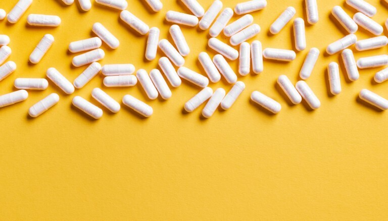 White medical capsules on bright yellow background, copy space. Drugs pattern. Medicine, dietary supplements, pharmacy and healthcare concept. Vitamin D3.