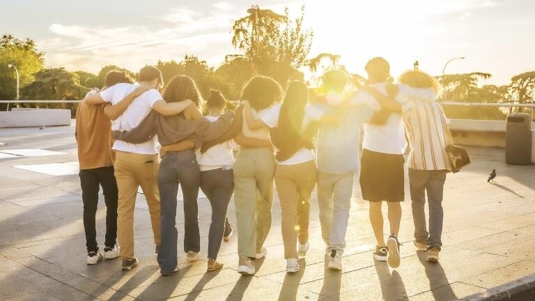 Rückansicht von Freunden, die sich umarmen und bei Sonnenuntergang gemeinsam durch die Stadt laufen