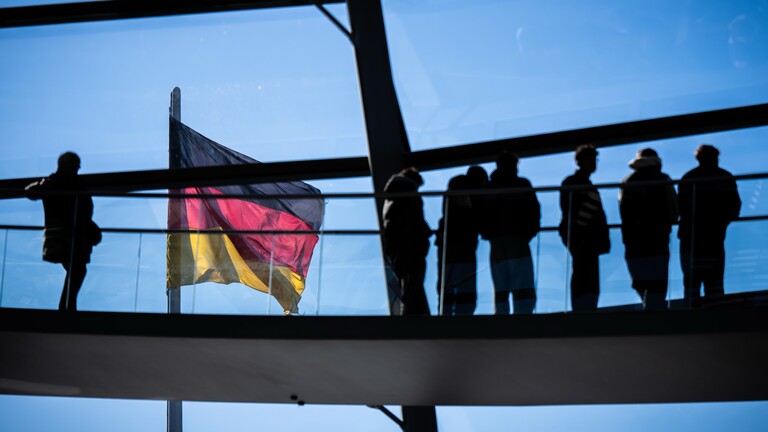 Besucher gehen vor der Deutschlandflagge in der Kuppel im Bundestag.
